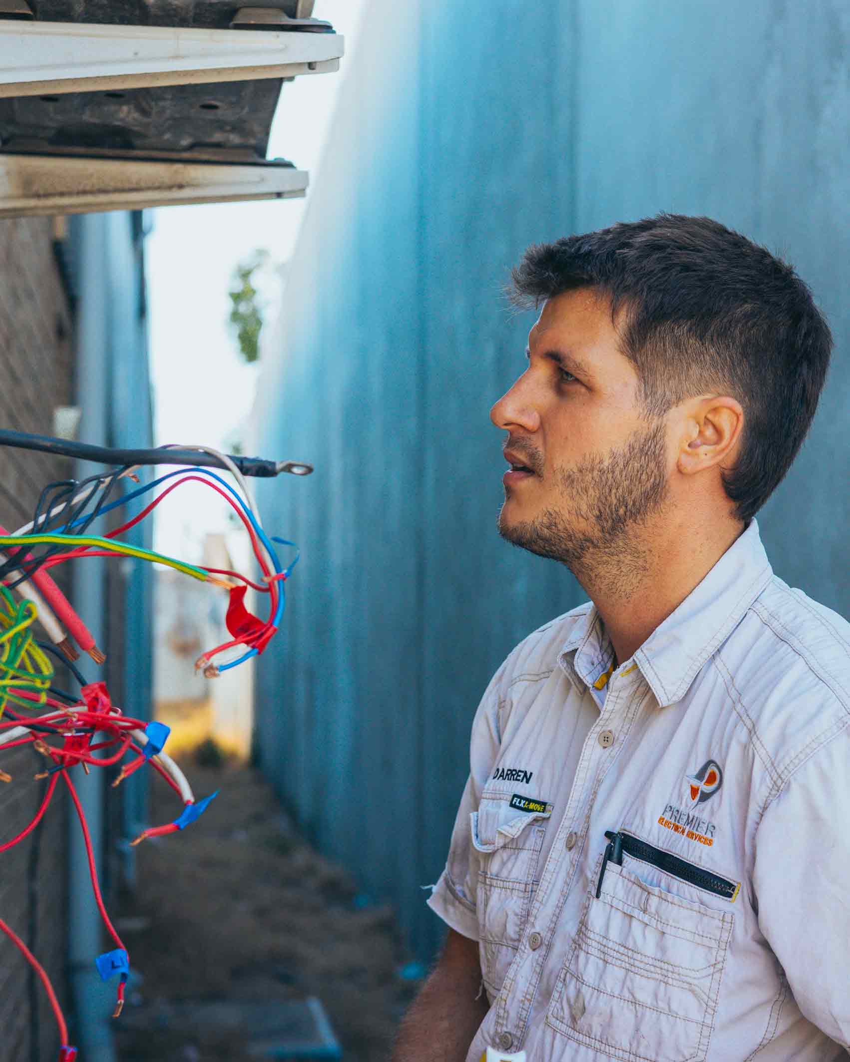 Electrical technician using a screwdriver to work on an outdoor electrical switchboard mounted on a white wall.