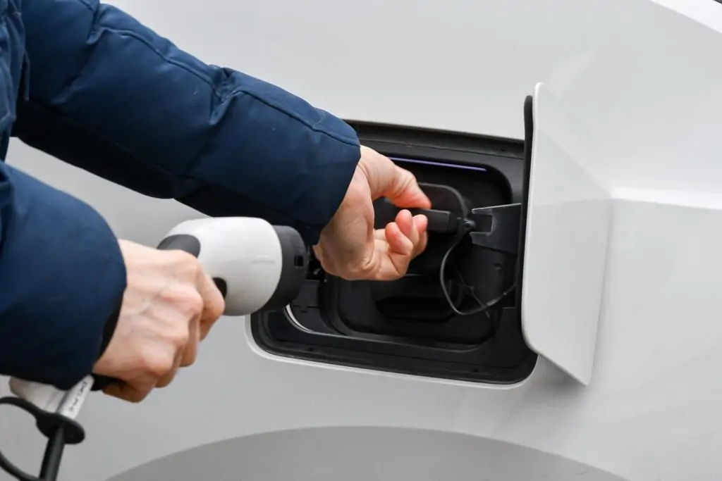 Electrical technician using a screwdriver to adjust an outdoor electrical panel mounted on a white brick wall.