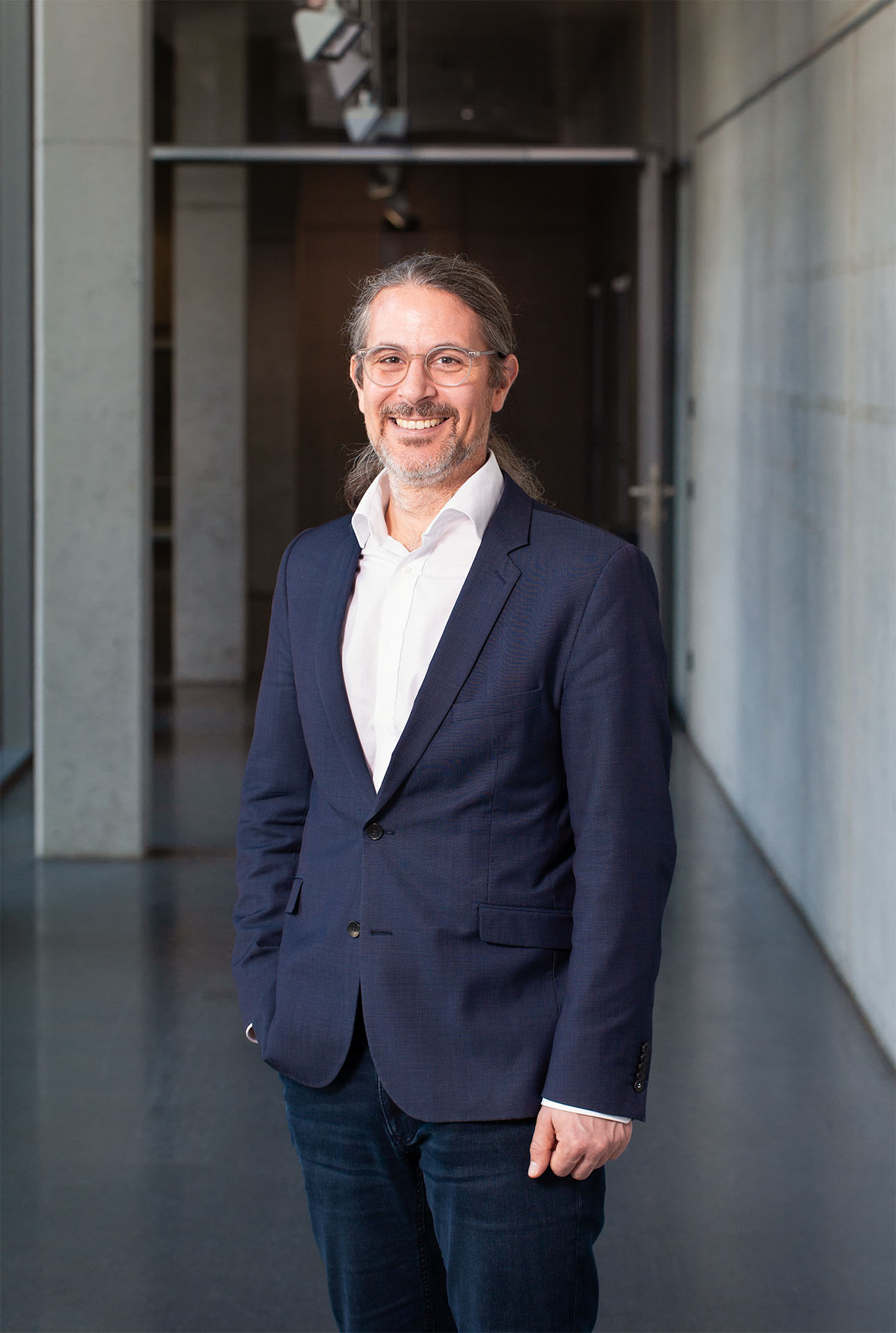 A middle aged man with beard and glasses in a suit is smiling