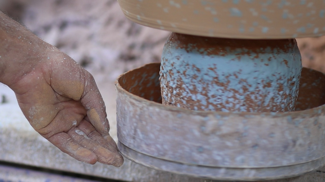 A hand touching a machine to paint ceramics