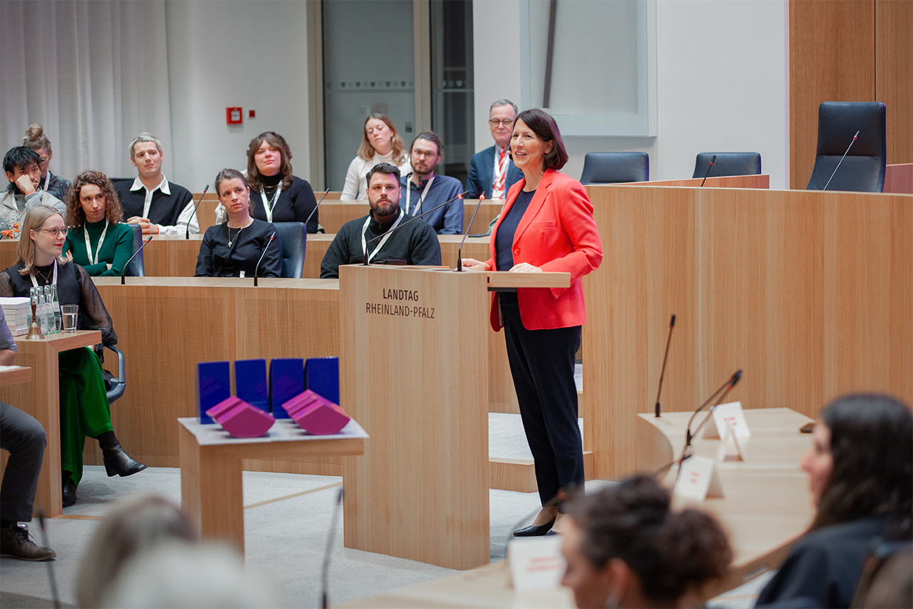 A man speaking into a microphone on an event. There are more people in the background