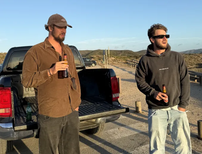 Two people standing outdoors talking near a car in the mountains