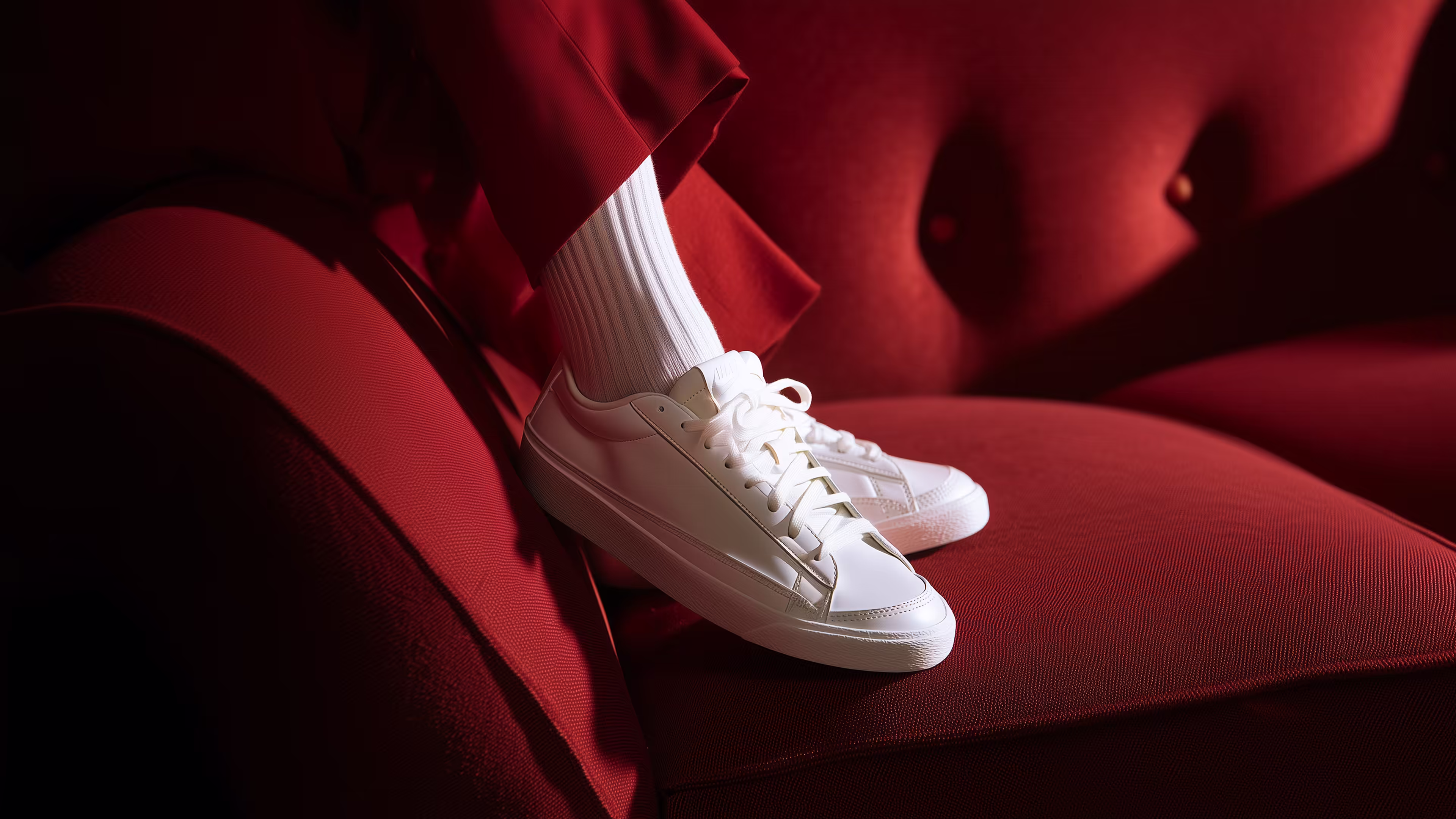 Person wearing white sneakers and white ribbed socks sitting on a red upholstered sofa.