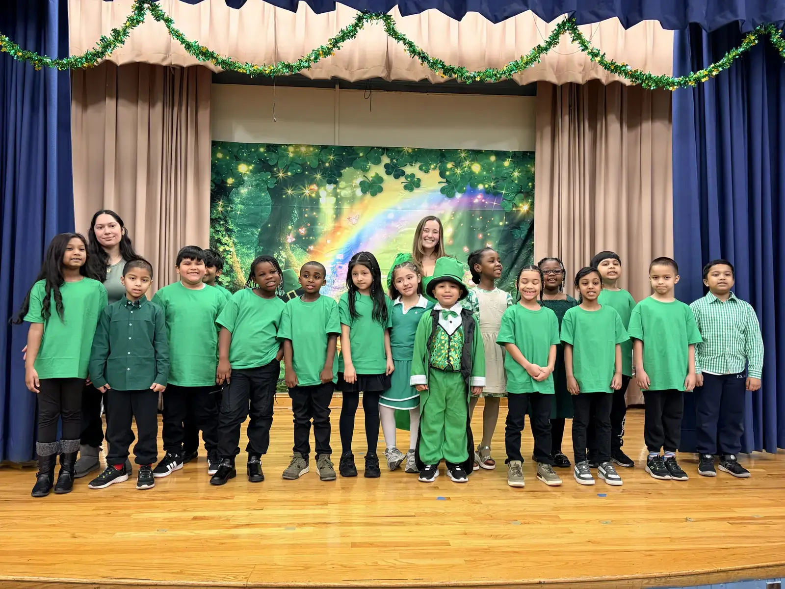 Students and teachers pose on stage in green costumes for Saint Patrick's Day performance