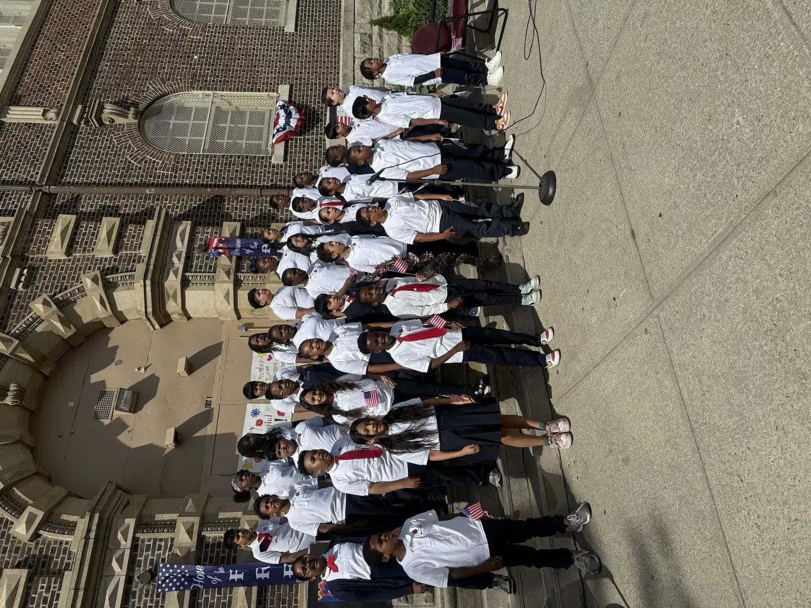 Students in uniform holding American flags outside school building