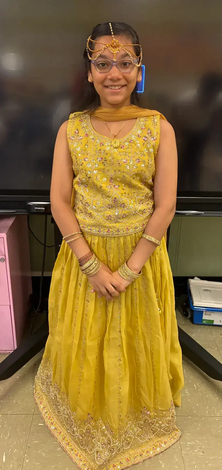 Student smiling in traditional yellow embroidered lehenga and gold jewelry