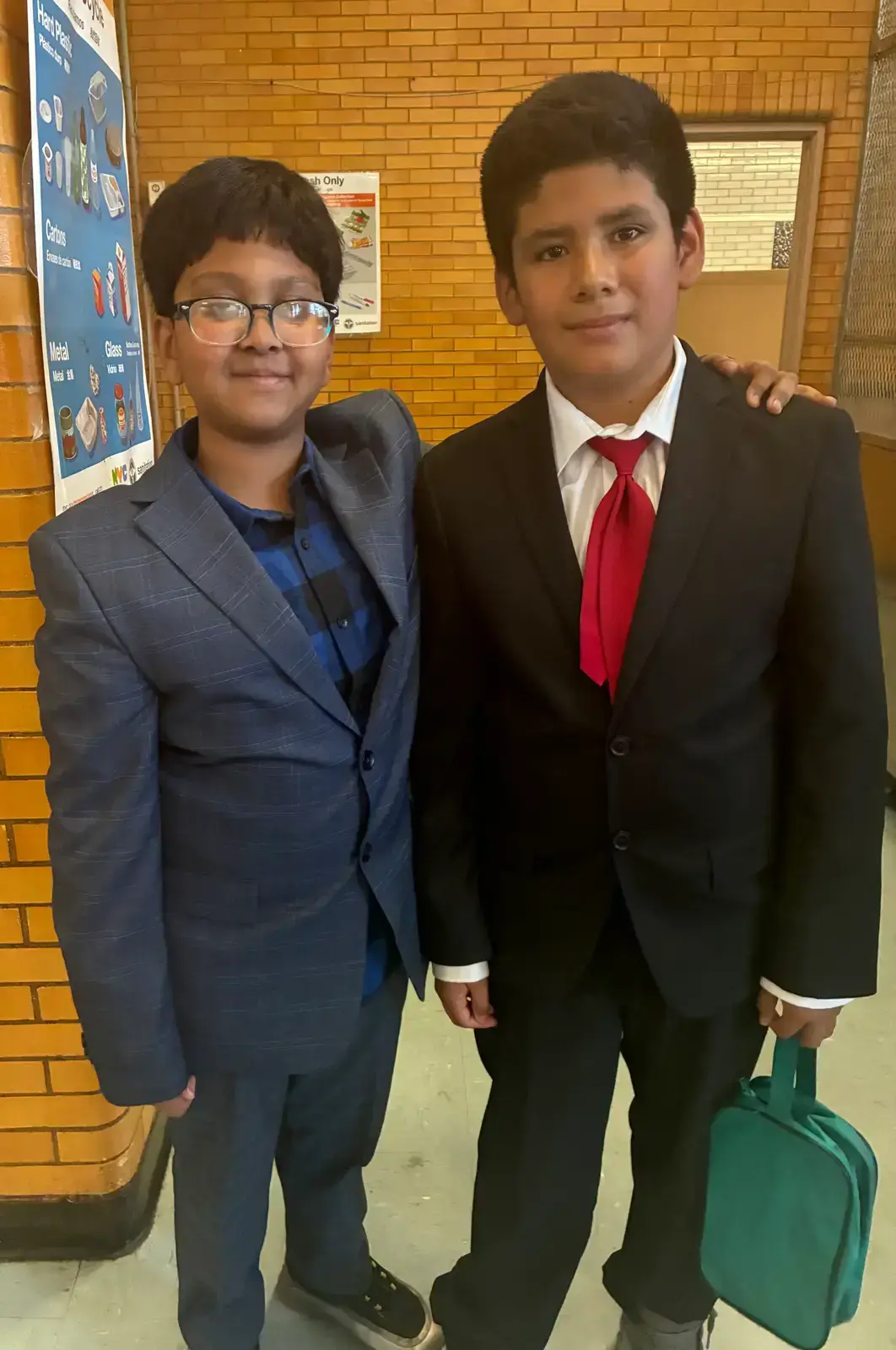 Two students dressed in suits posing together in school hallway