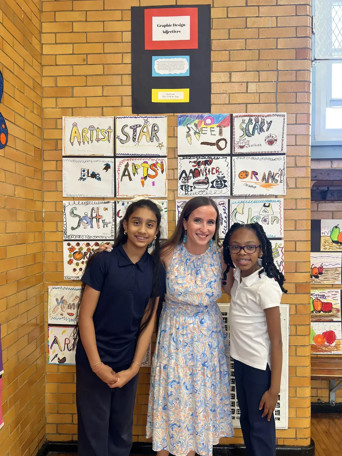 Teacher and two students posing beside graphic design adjectives artwork display