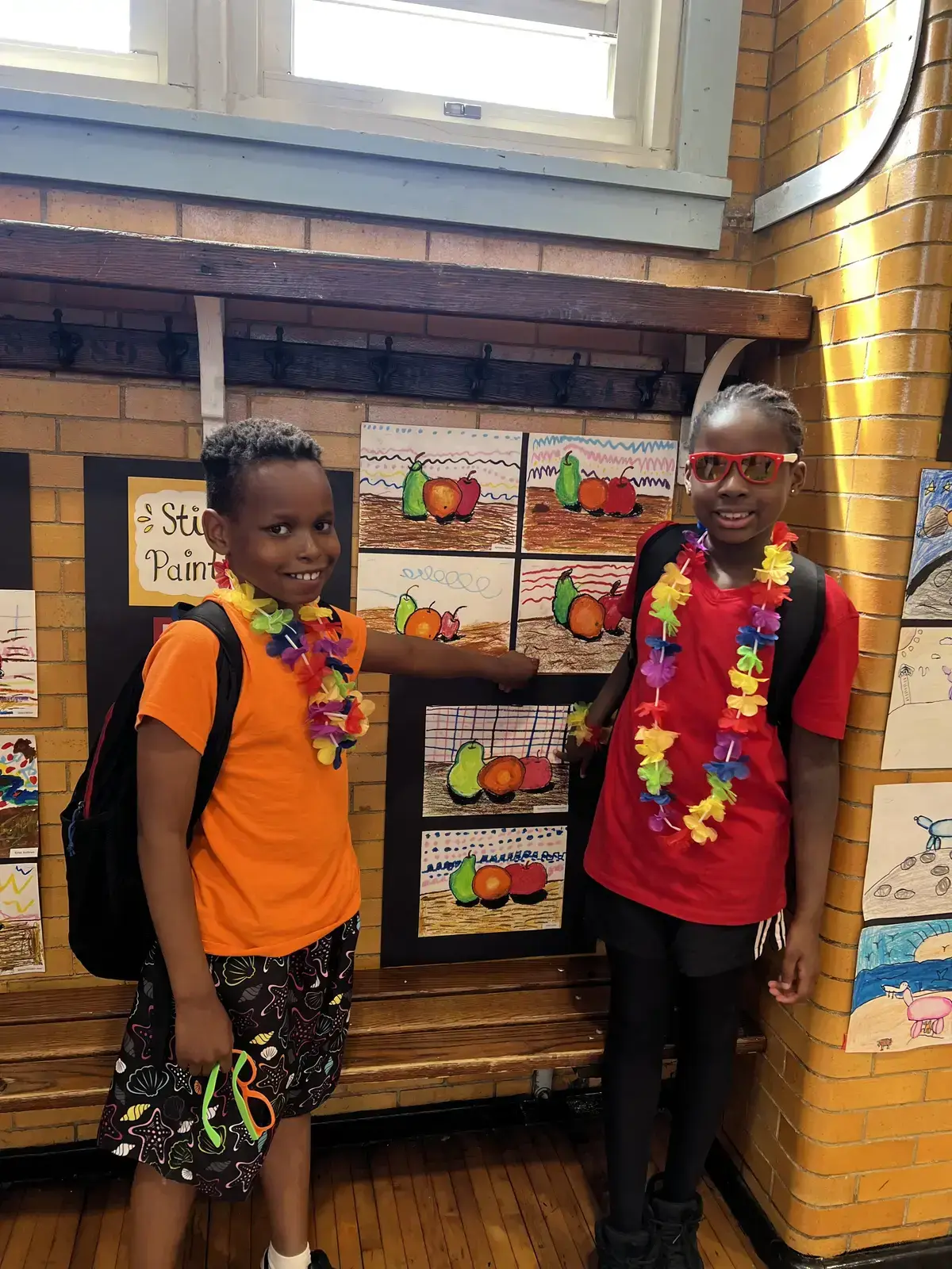 Two students proudly displaying their still life fruit paintings at school art show