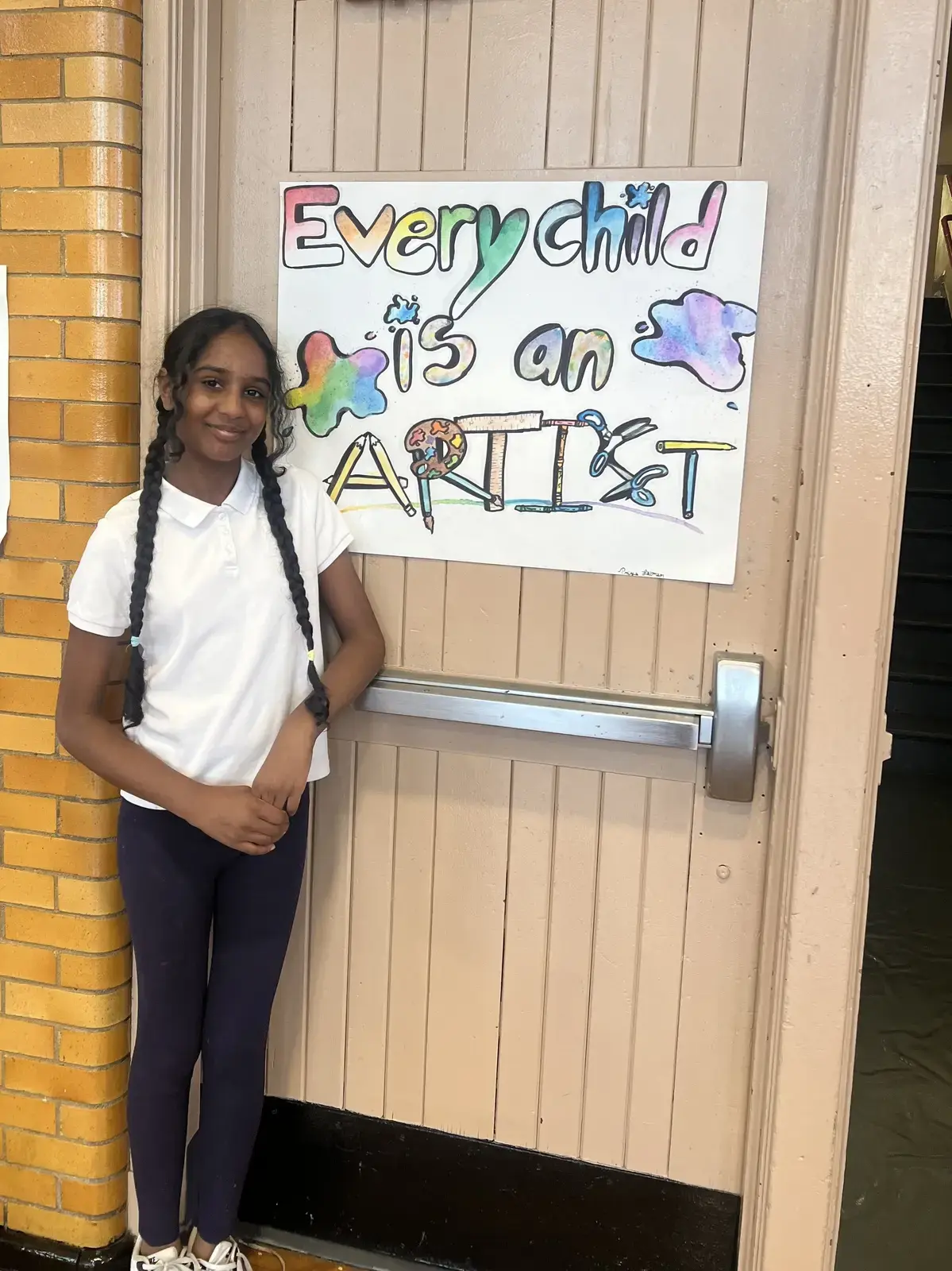 Student posing beside her Every Child Is an Artist poster