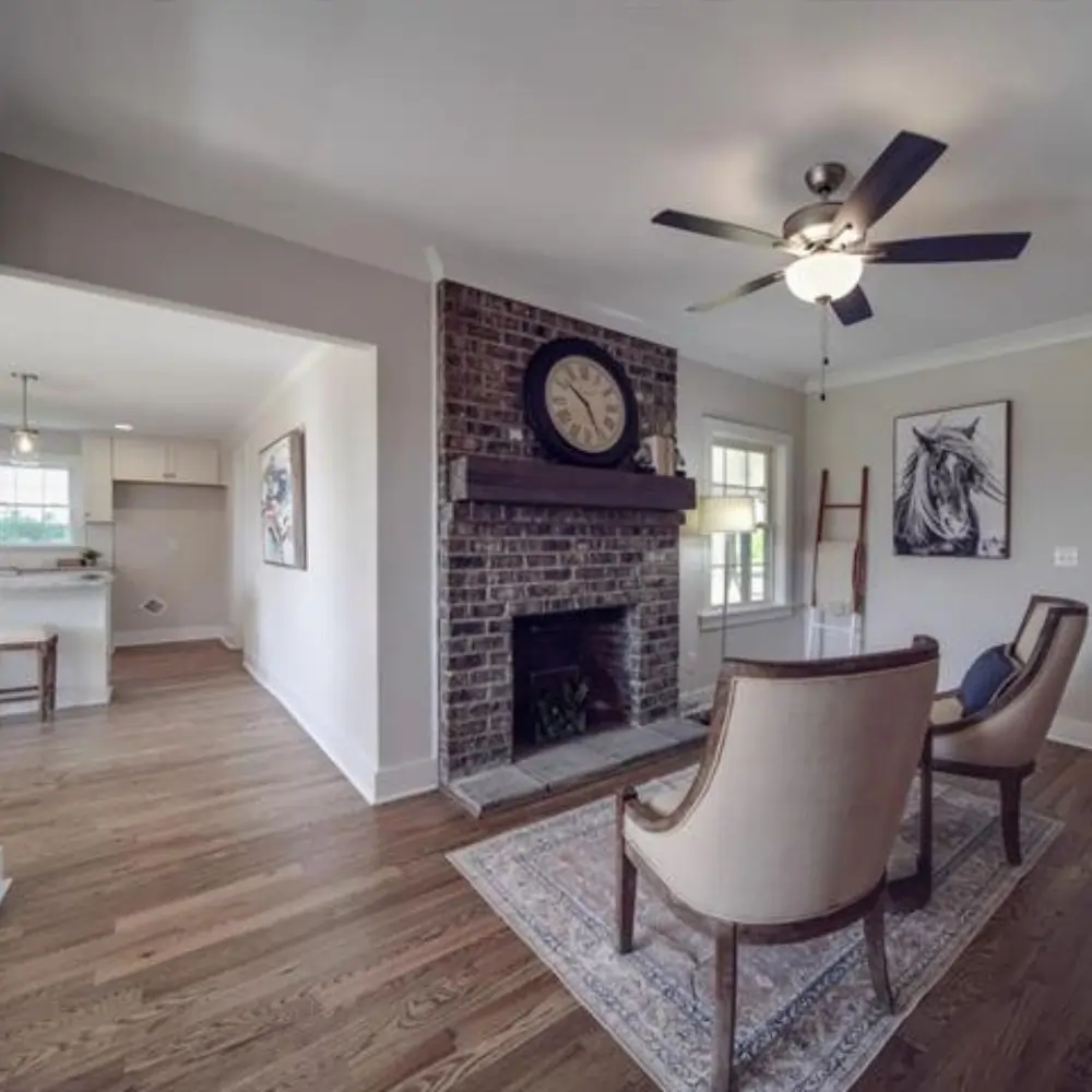 Cozy sitting area with brick fireplace, hardwood floors, and view into bright kitchen.