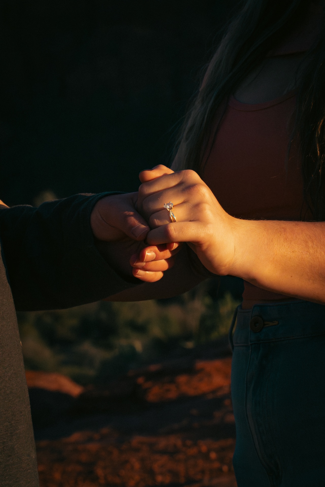 Close-up of two people holding hands, with one person wearing an engagement ring.