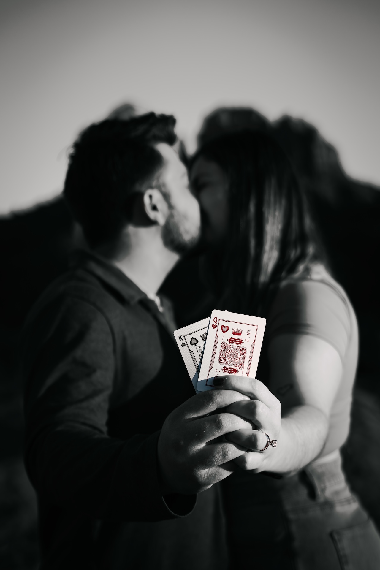 Couple kissing with focus on their hands holding a king of spades and queen of hearts playing cards.