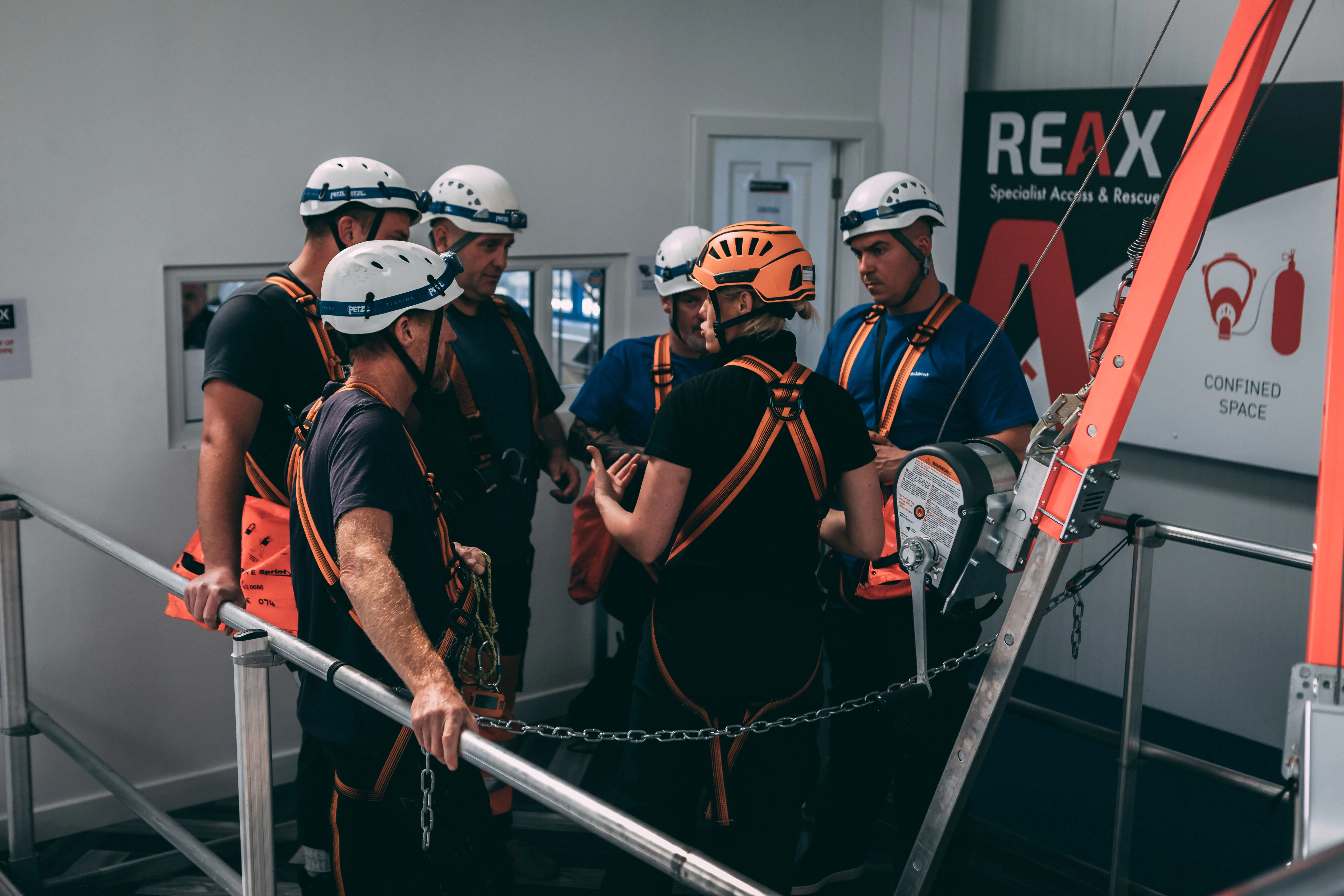A group of participants wearing safety helmets and harnesses surrounding the instructor who is explaining instructions to the group