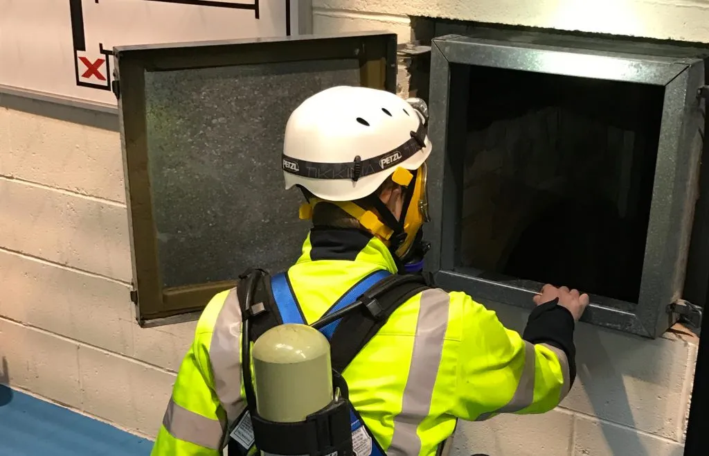 A worker in protective gear examining a confined space