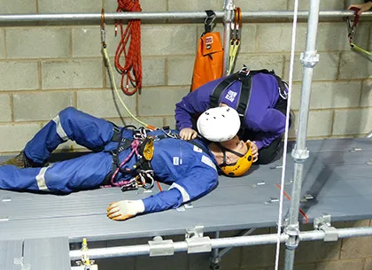 A person performing CPR on a casualty as part of first aid training. The casualty is lying on the ground and the person is kneeling beside it, pressing down on the chest with their hands and tilting the head back to administer breaths