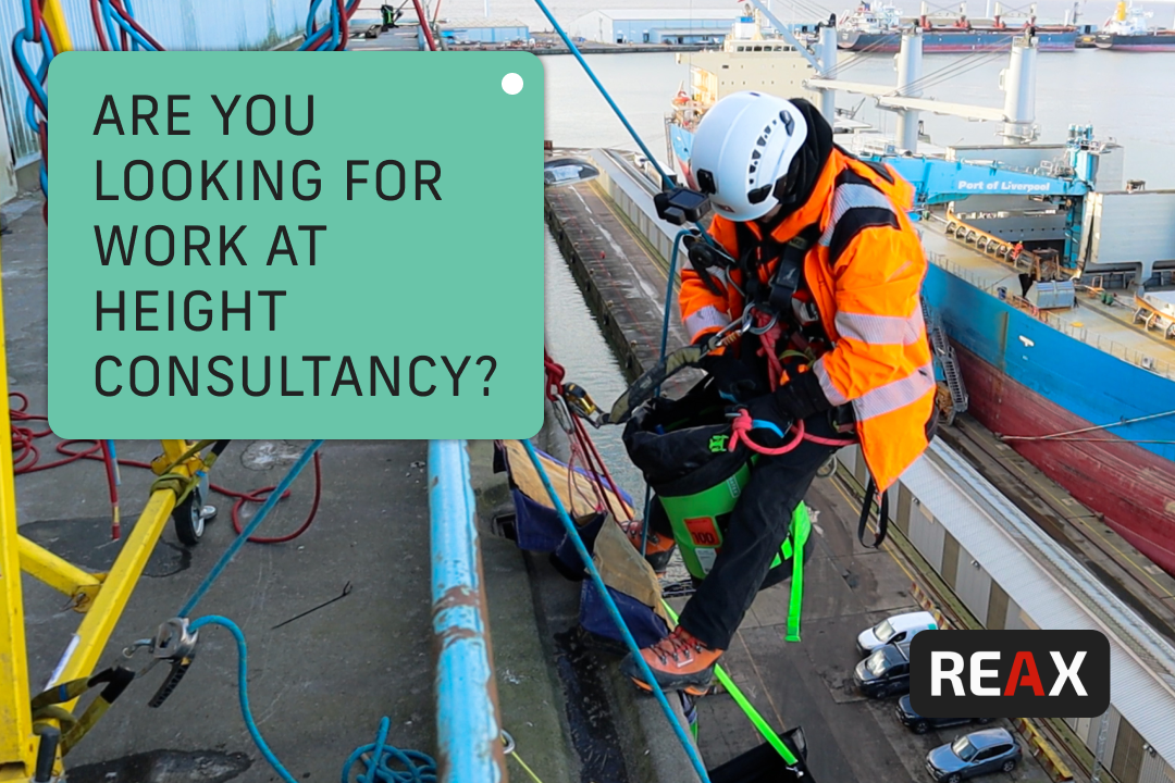 A man in an orange jacket is suspended from a rope, appearing to be engaged in a climbing or rescue activity.