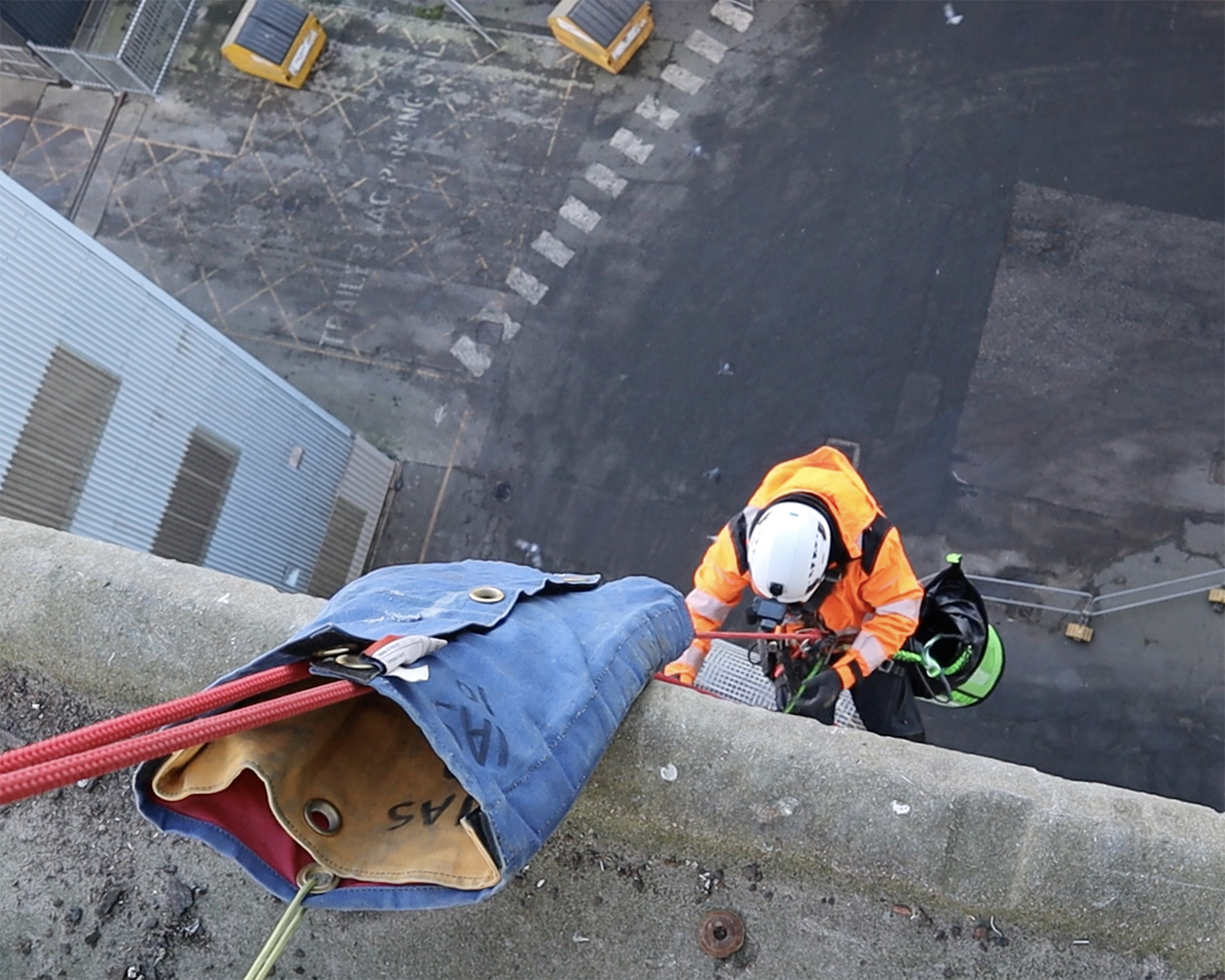 A man in an orange vest is working on a building, focused on construction tasks.