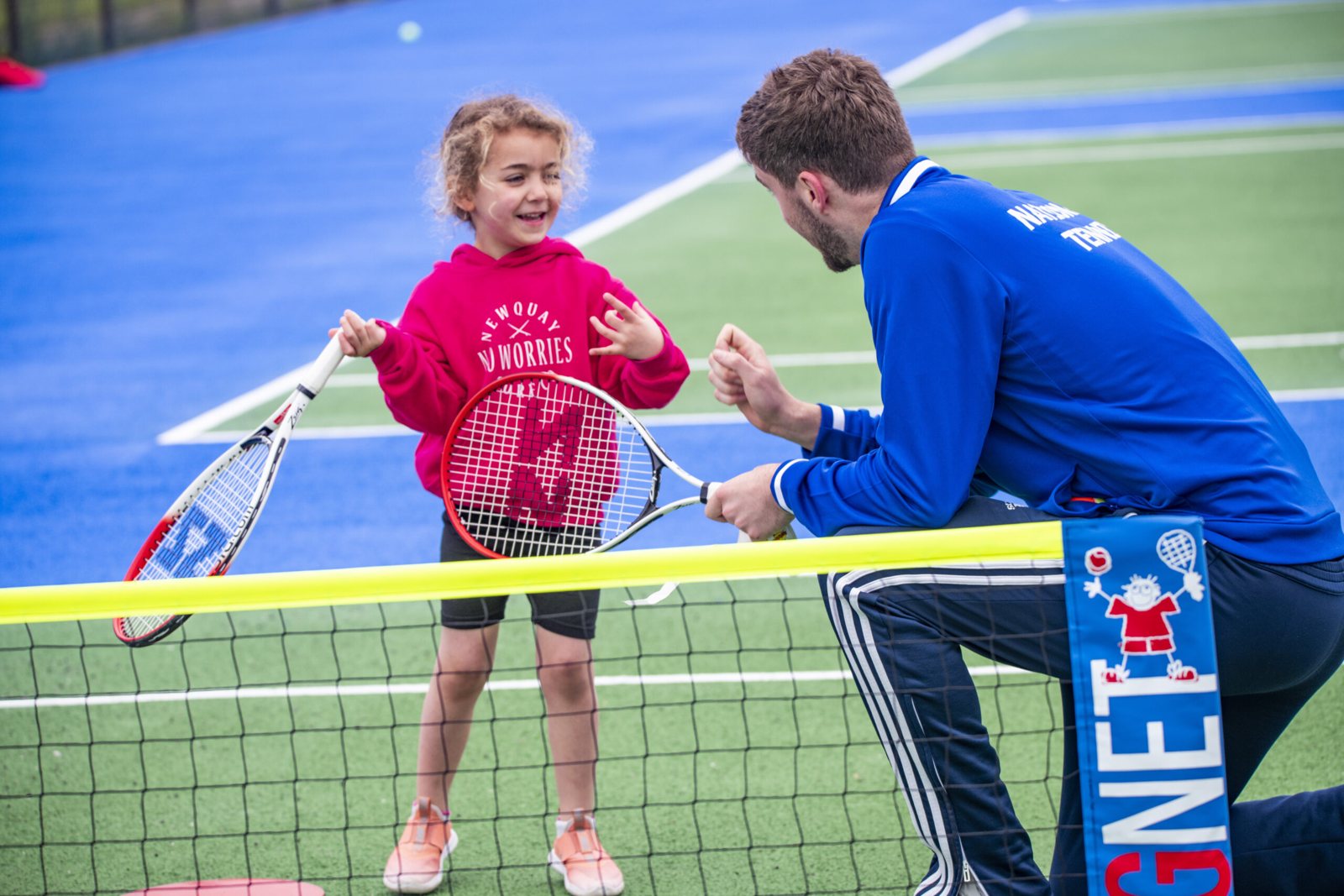 National Tennis coach encouraging a young player at a mini tennis net