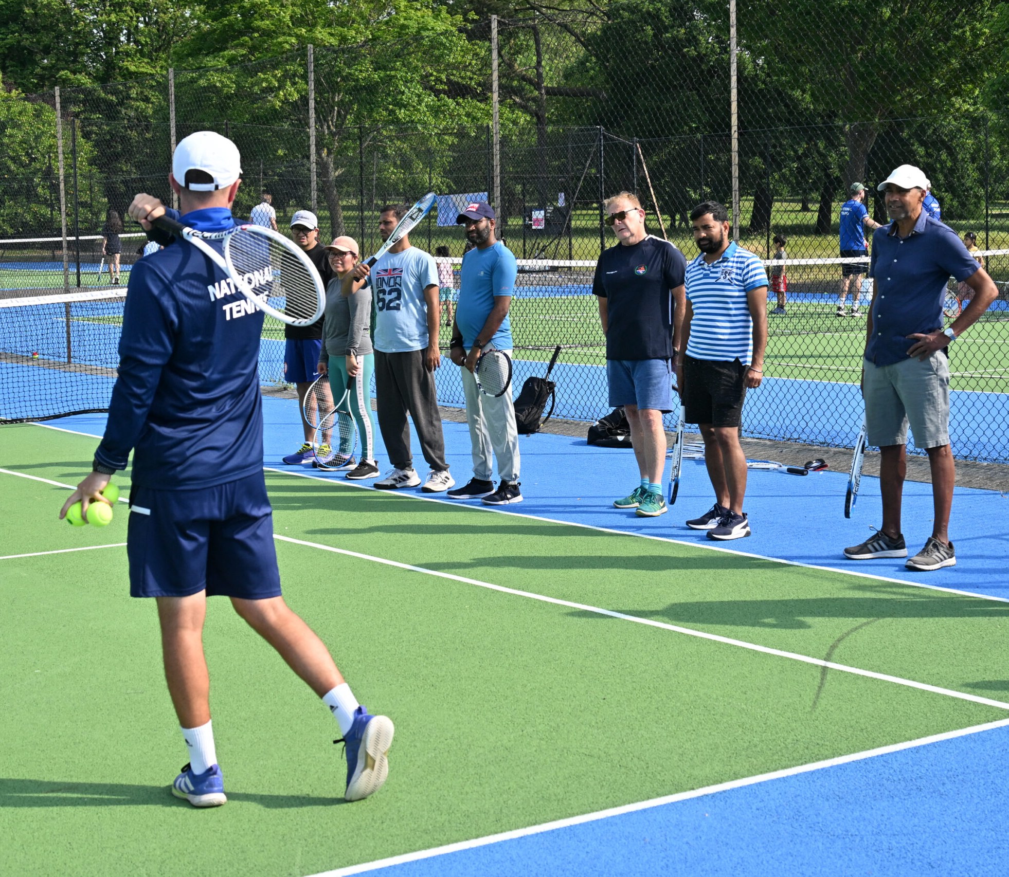 A National Tennis coach leading an adult group session on a park court