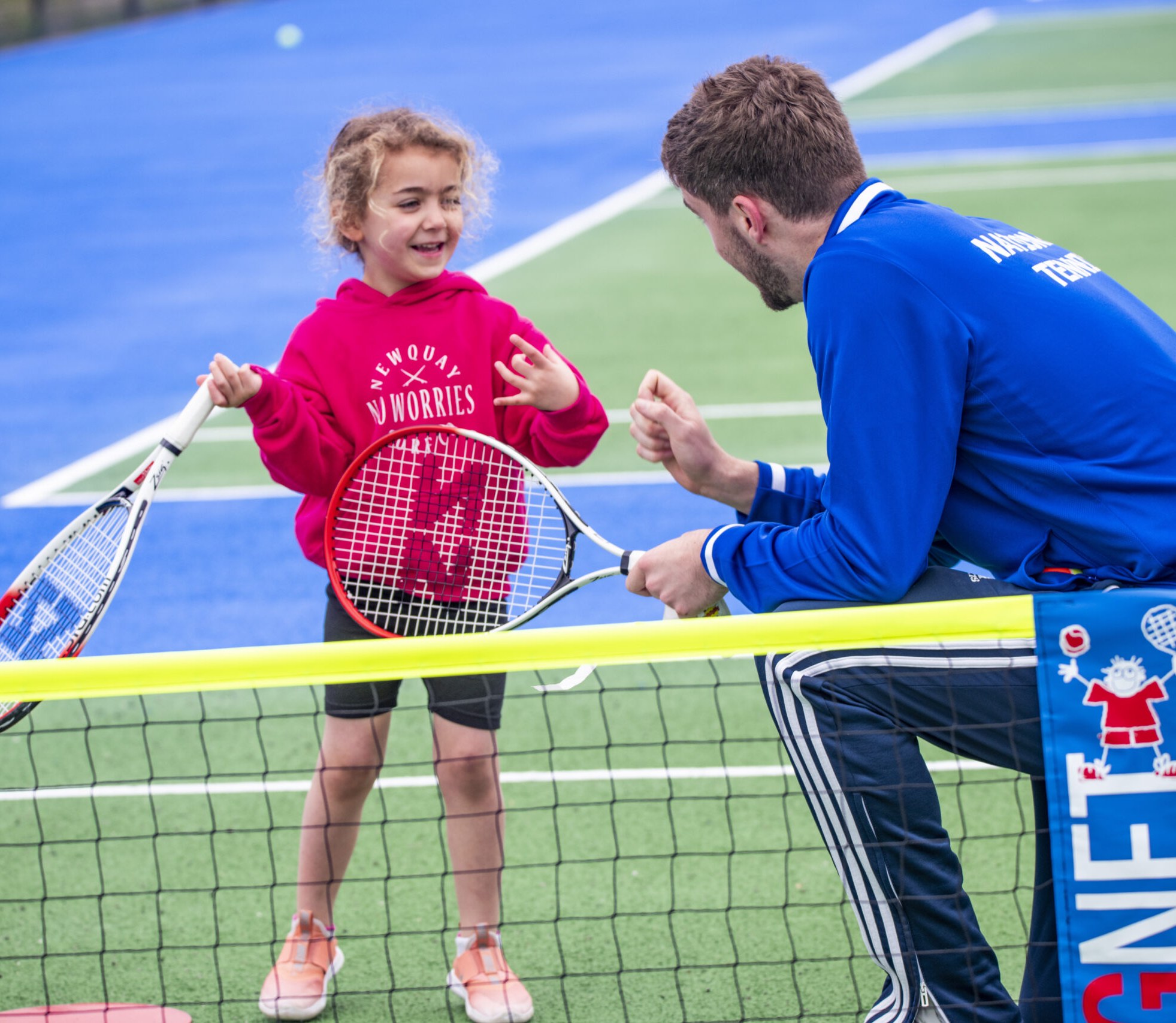 A young player laughing with a National Tennis coach at the net