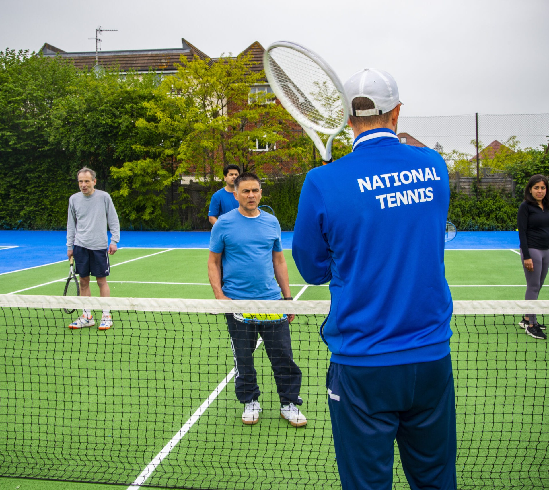 A National Tennis coach running a group session on a park court