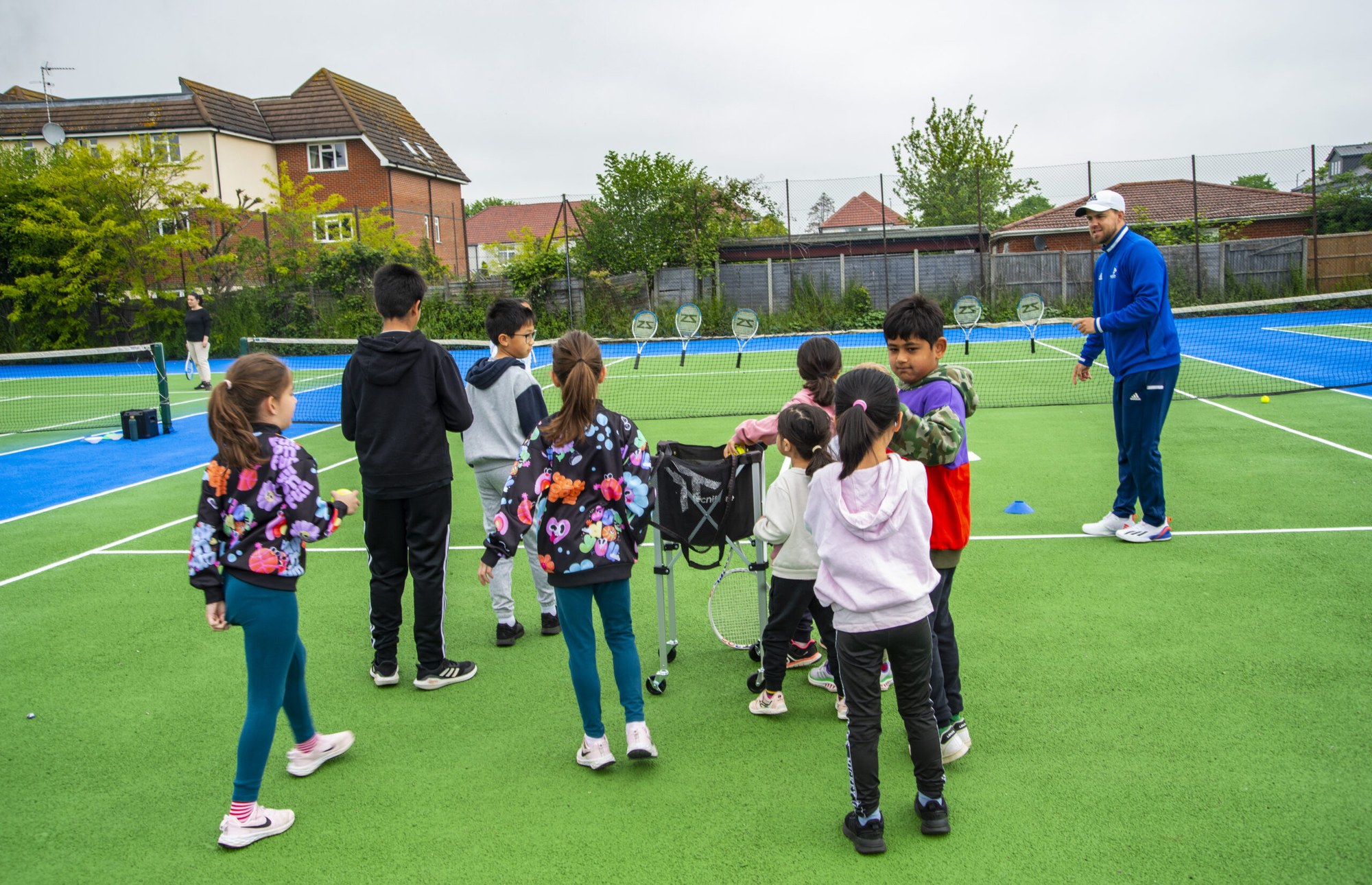 A coach leading a group of young players in a game at a tennis camp
