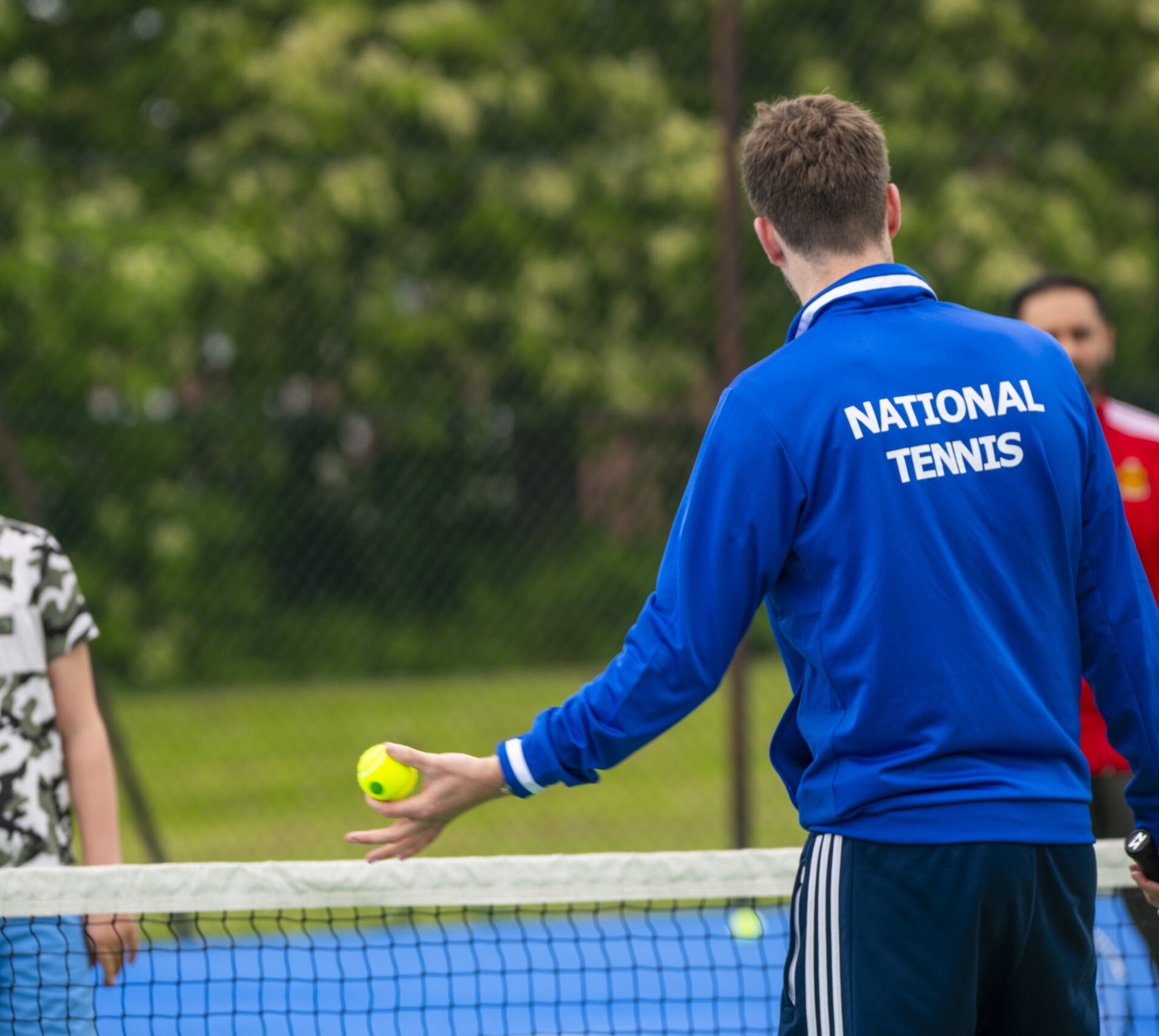 A National Tennis coach working with a young player at the net
