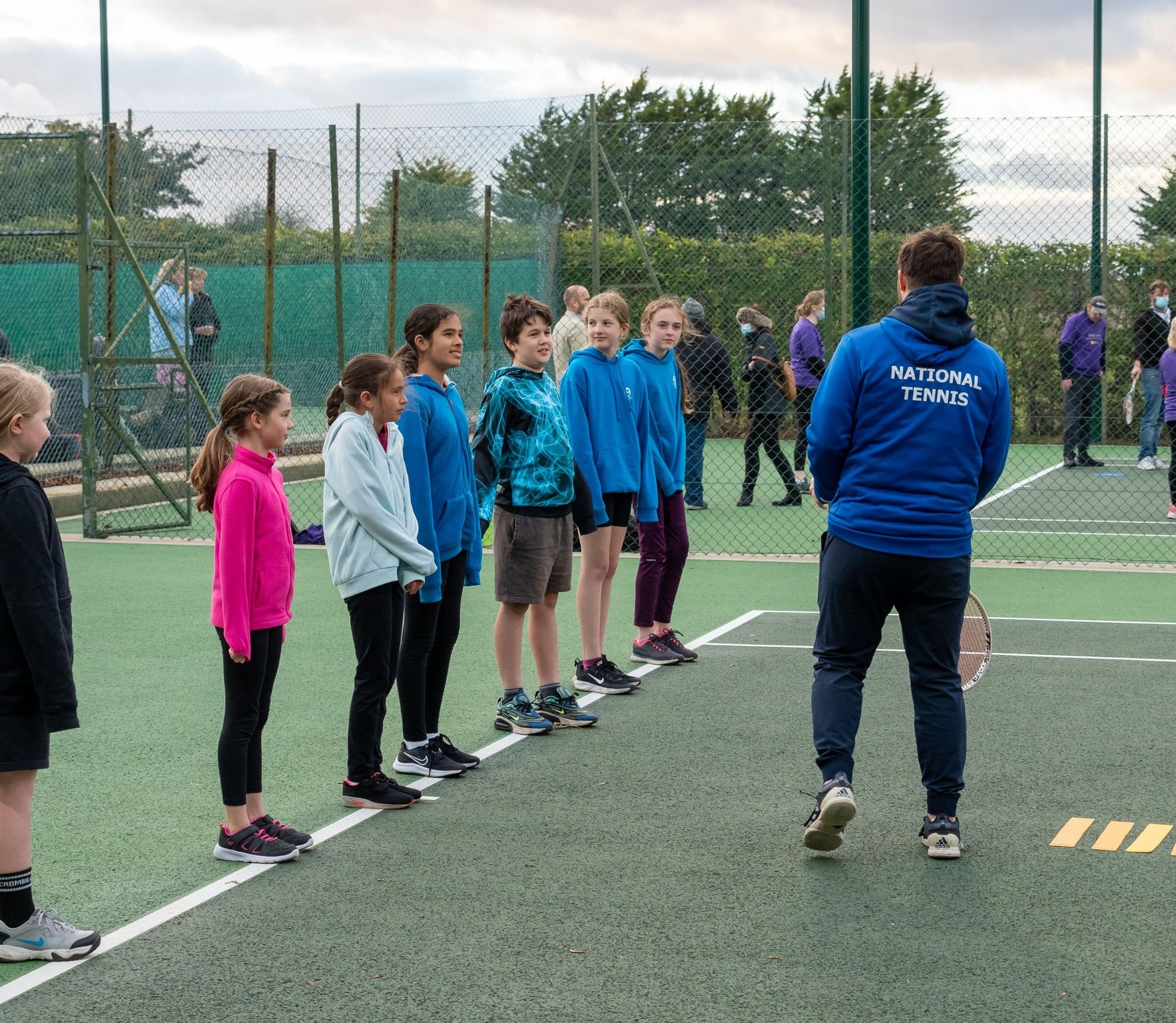 A National Tennis coach with a line of young players at a weekly session