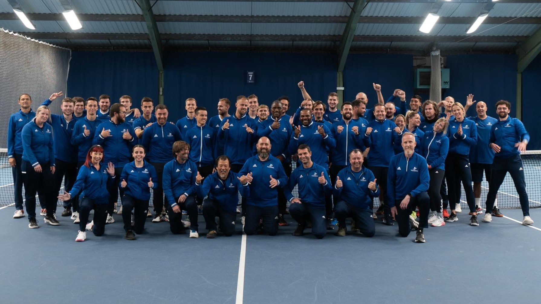 The National Tennis coaching team in matching blue kit, celebrating together on an indoor court