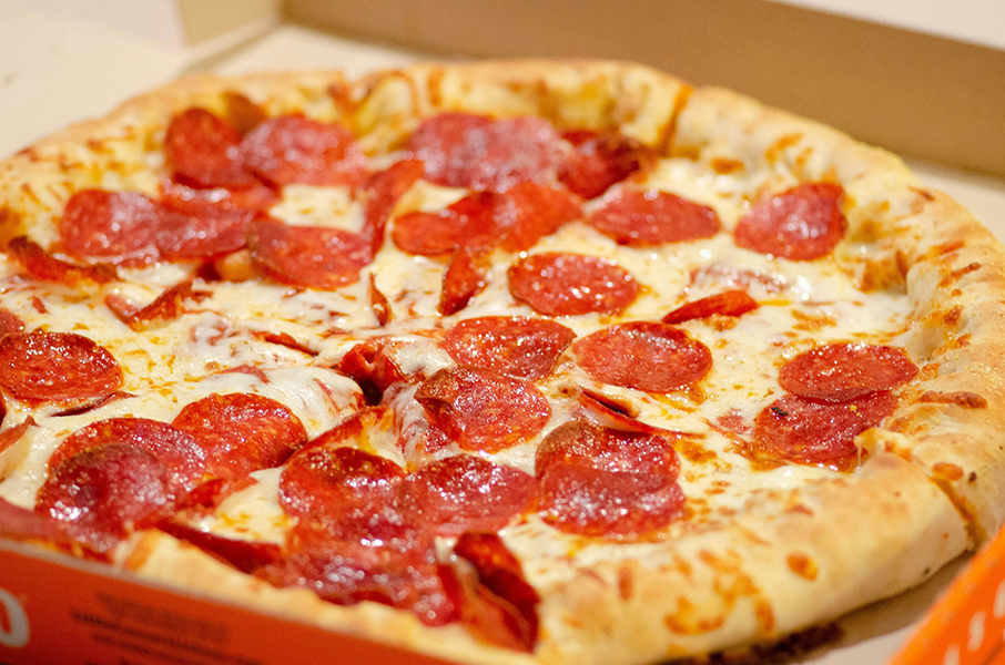 Freshly baked pepperoni pizza with melted cheese, arranged on a cardboard box. The pizza is golden brown with a sizzling appearance, evoking appetite.