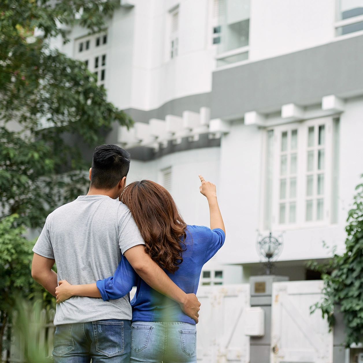 Couple embracing and looking at a modern white house, with the woman pointing towards the building.
