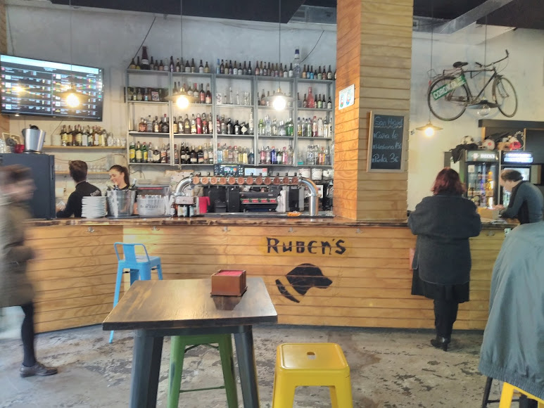 Interiores del bar Rubens con barra de madera y personas de pie en la barra.
