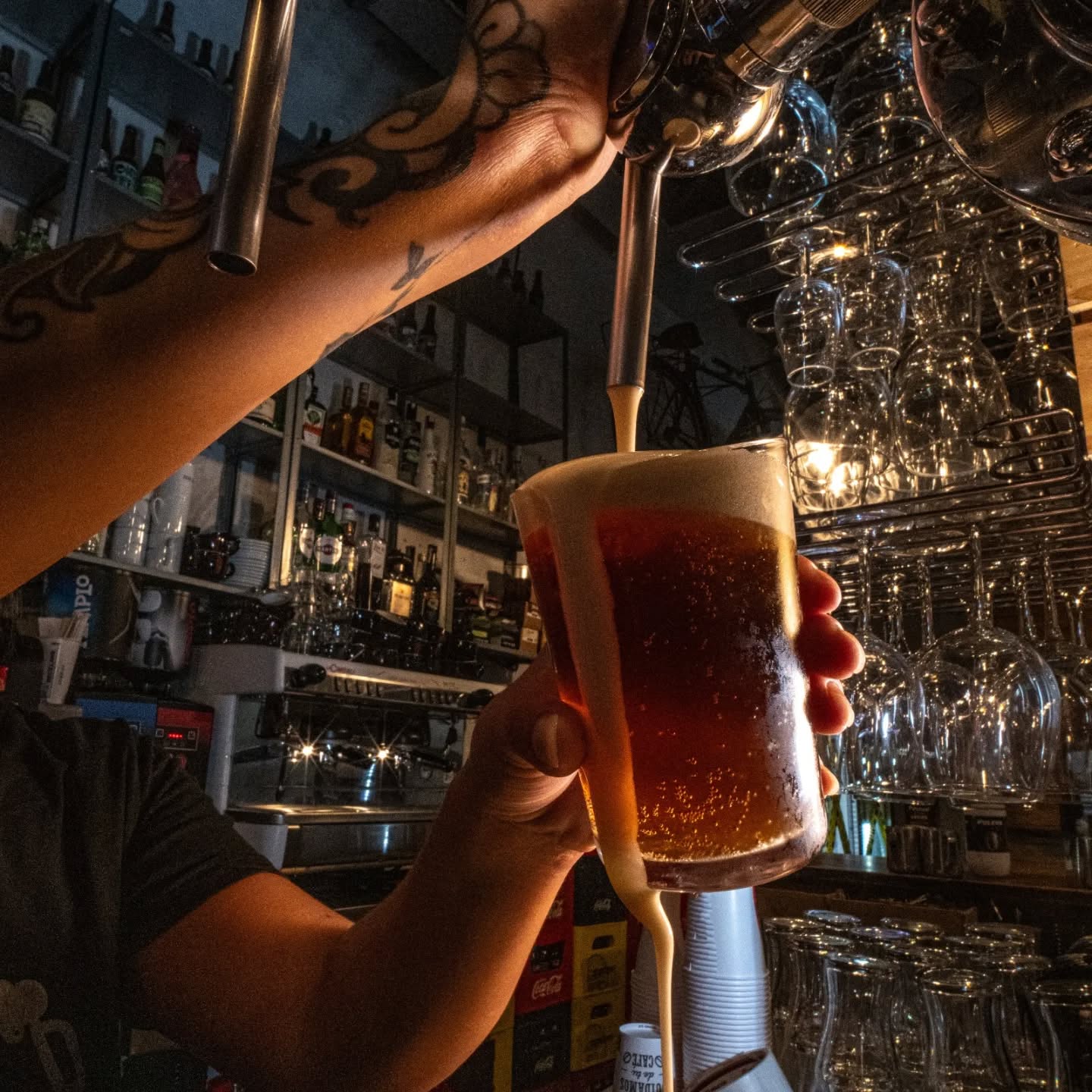 Persona sirviendo una cerveza oscura con espuma en un vaso en un bar.