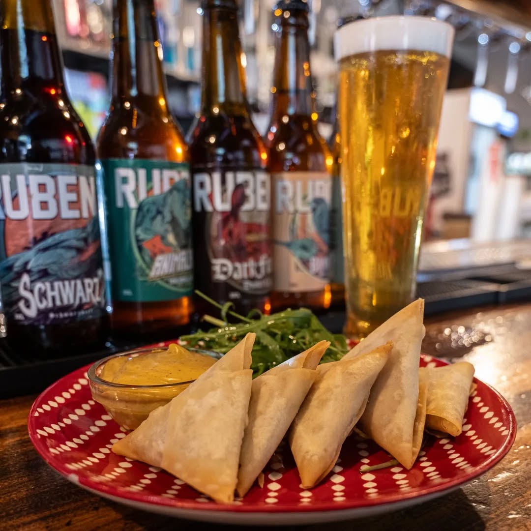 Plato con comida para compartir, con varias botellas de cerveza y un vaso de cerveza.