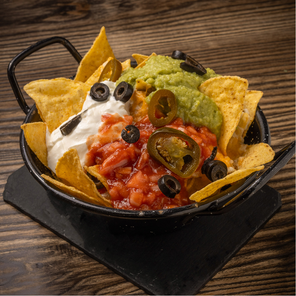Bandeja de nachos con guacamole, salsa roja, crema agria y jalapeño.
