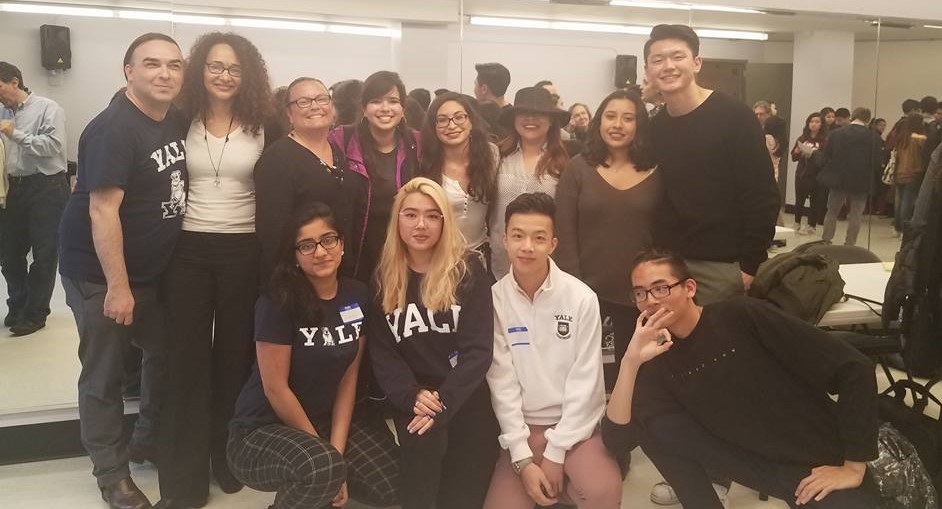 Group of diverse young adults smiling and posing together indoors, some wearing Yale sweatshirts.