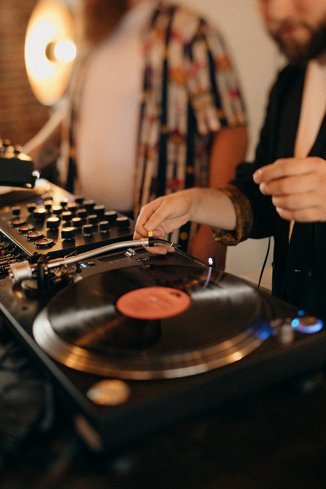 Zbliżenie na gramofon i mikser; ręce DJ-a ustawiają ramię i gałki podczas miksowania.