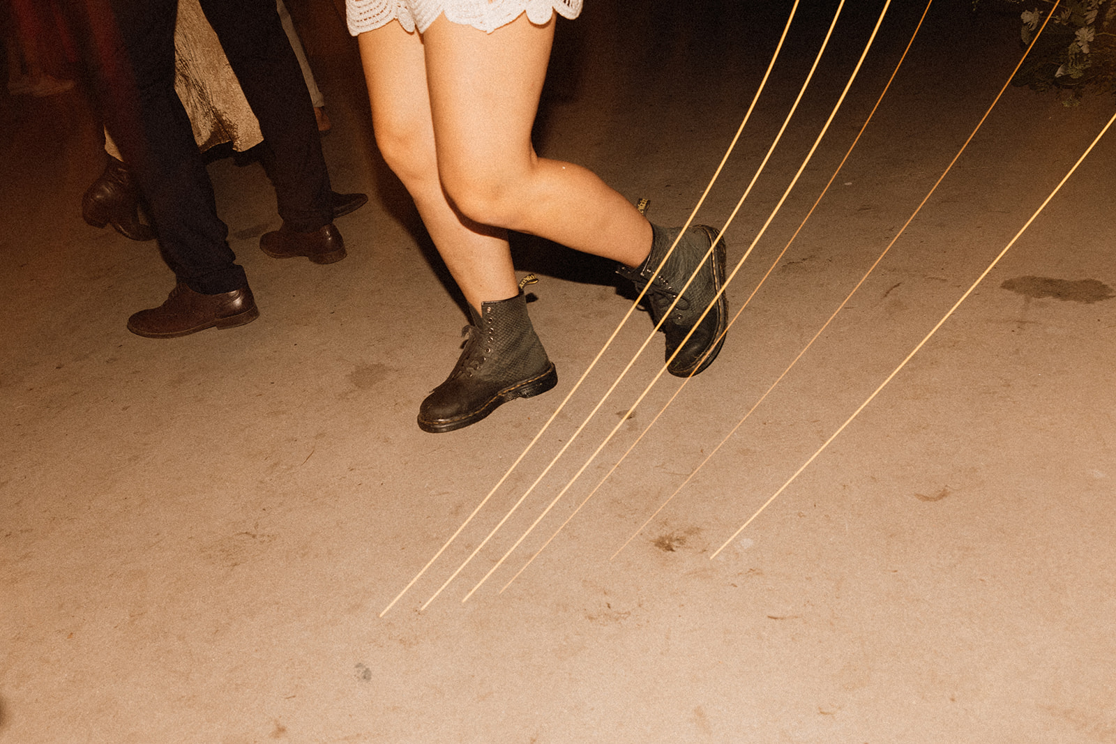 Zbliżenie na nogi tancerki w czarnych butach typu glany w ruchu; smugi światła podkreślają dynamikę.