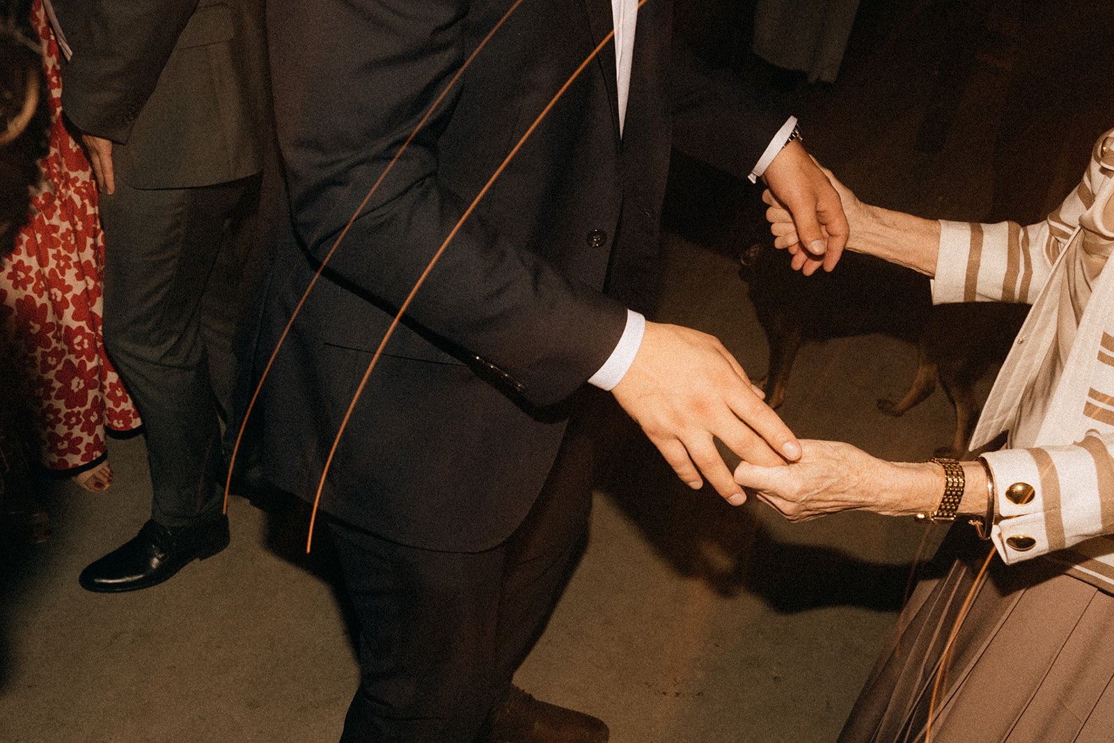 Zbliżenie na ręce dwóch osób trzymających się podczas tańca; elegancki garnitur i bransoletka w kadrze.