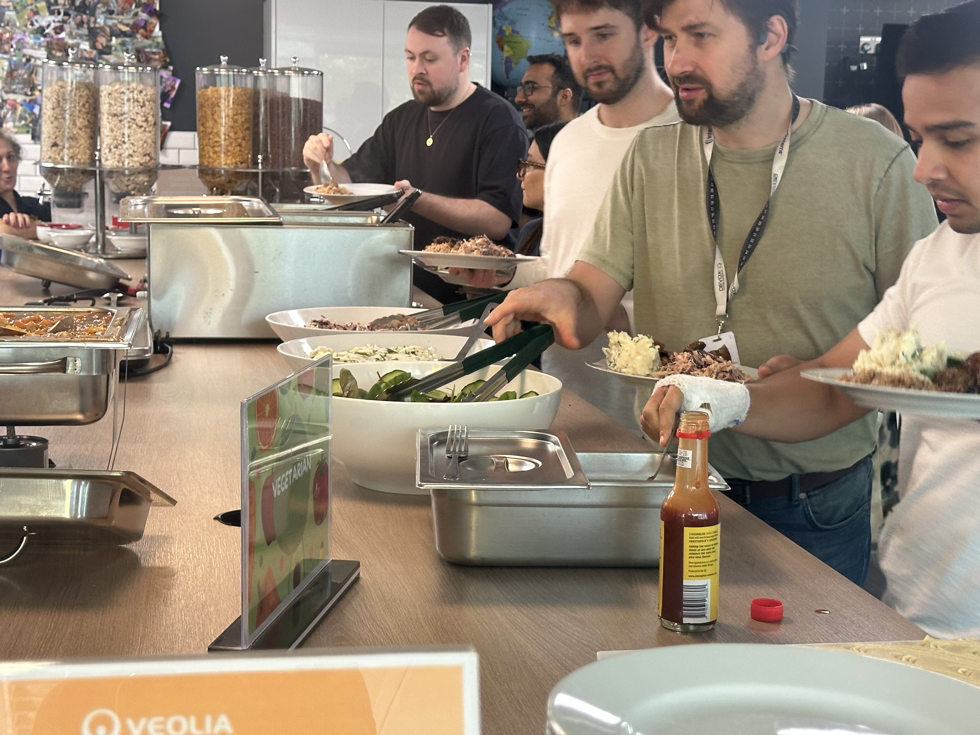 People serving themselves food from a buffet line with various dishes, including salad and hot food trays.