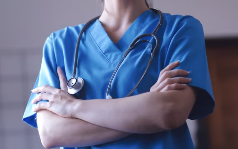 A woman in a blue scrub suit with a stethoscope on her arm.