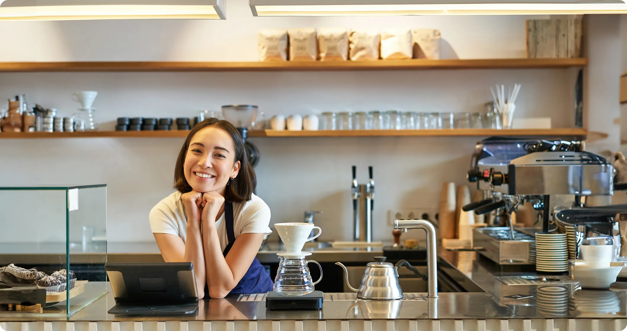 Smiling barista in apron behind counter with coffee equipment and pastries