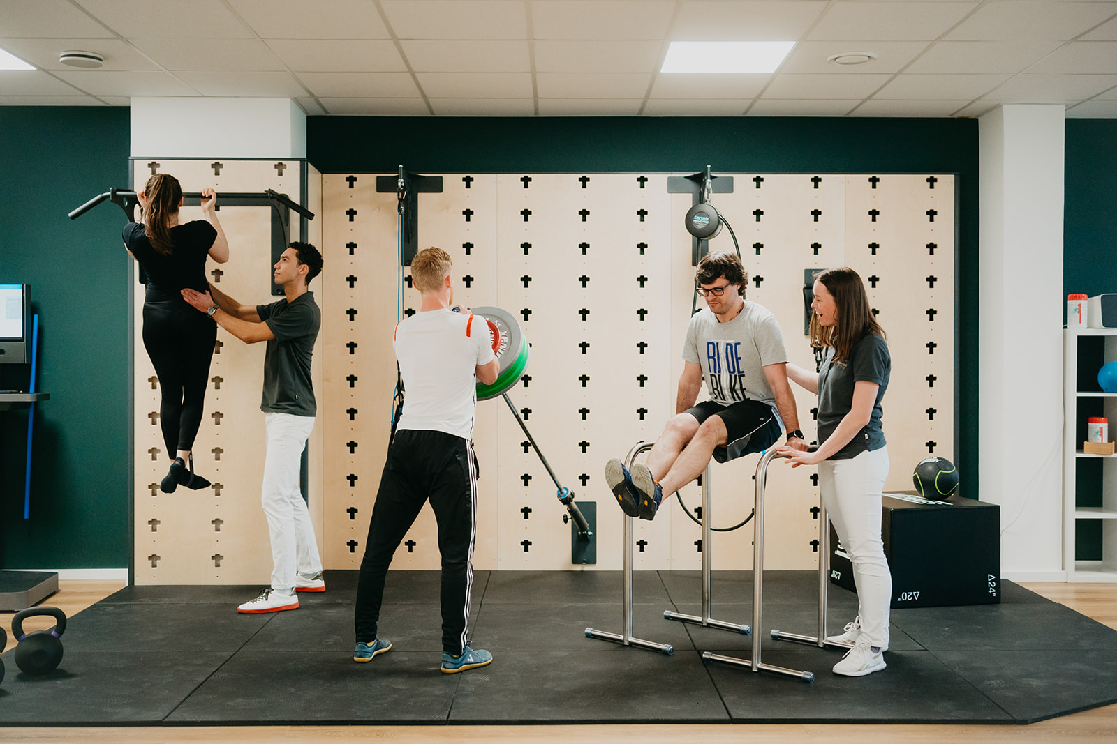Zwei Physiotherapeuten unterstützen zwei Patienten bei Fitnessübungen in einem modernen Therapiezentrum.