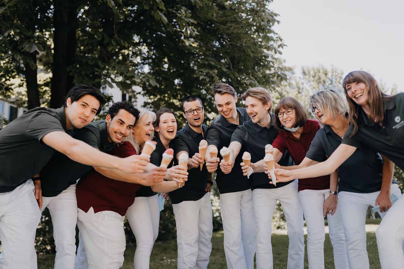 Ein Team von neun Menschen vor Bäumen steht mit Eiscreme und lächelt gemeinsam in die Kamera.