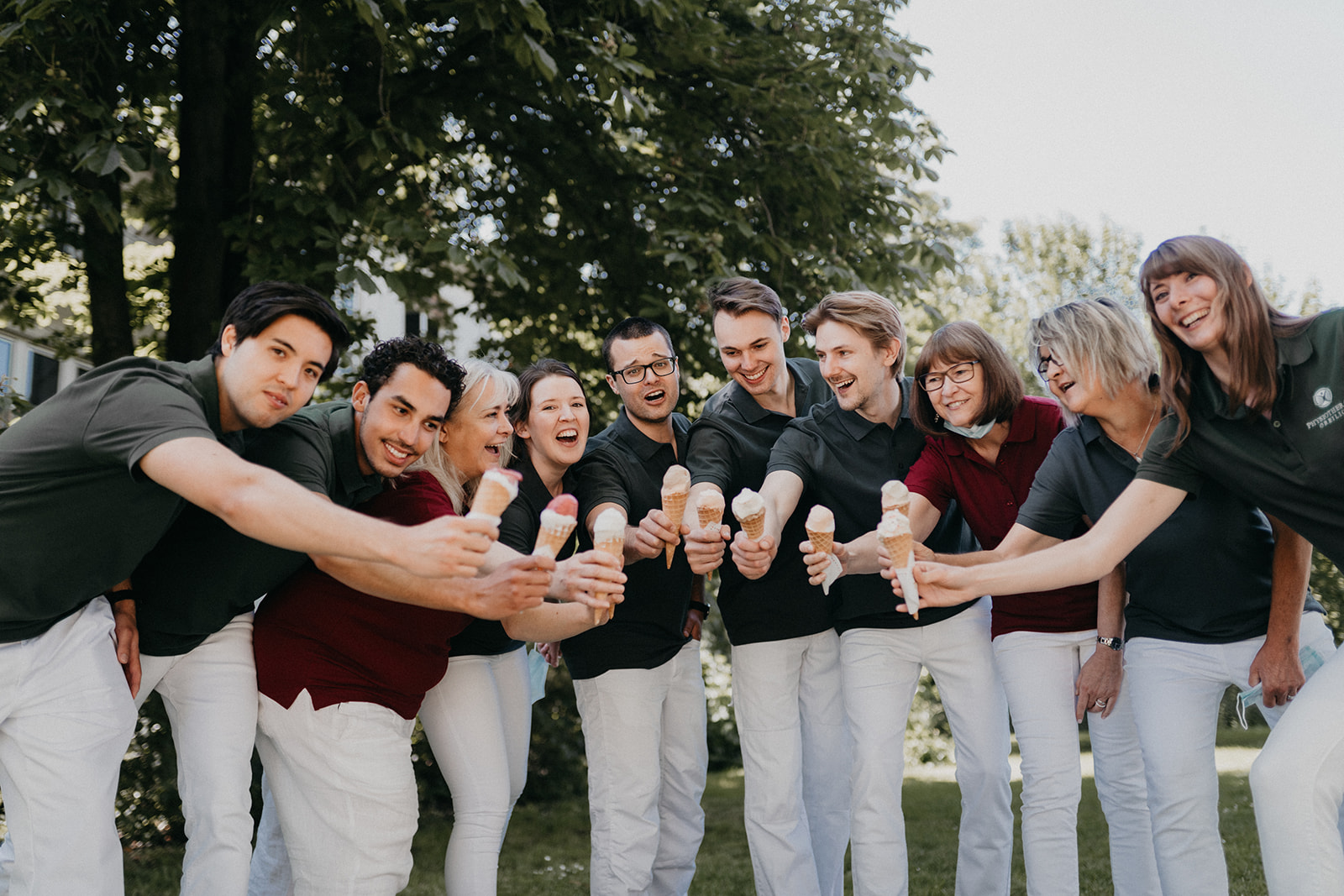 Ein Team von neun Menschen vor Bäumen steht mit Eiscreme und lächelt gemeinsam in die Kamera.