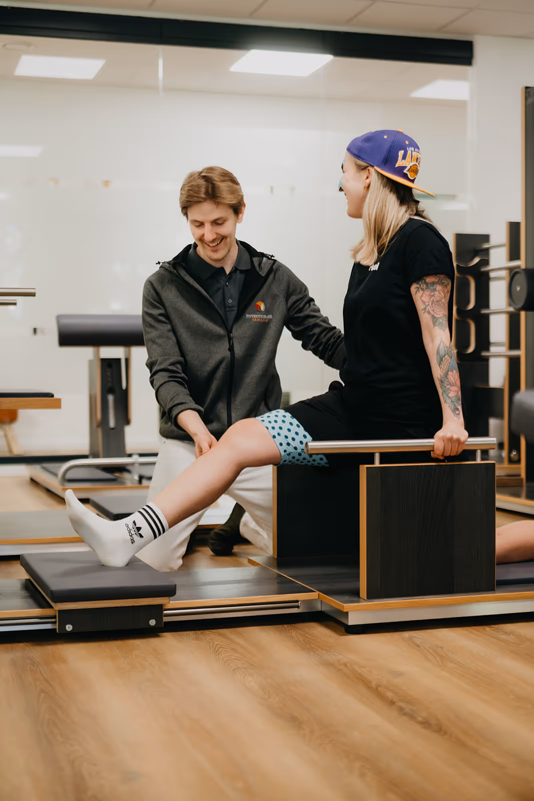 Physiotherapeut begleitet eine Patientin bei einer Beinübung auf einem Reformer-Gerät im Fitnessstudio.