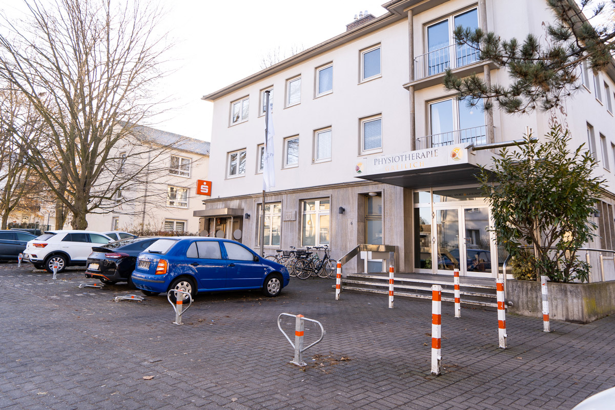 Außenansicht eines Gebäudes mit Eingang zur Physiotherapie Greilich, davor parkende Autos und Fahrräder.