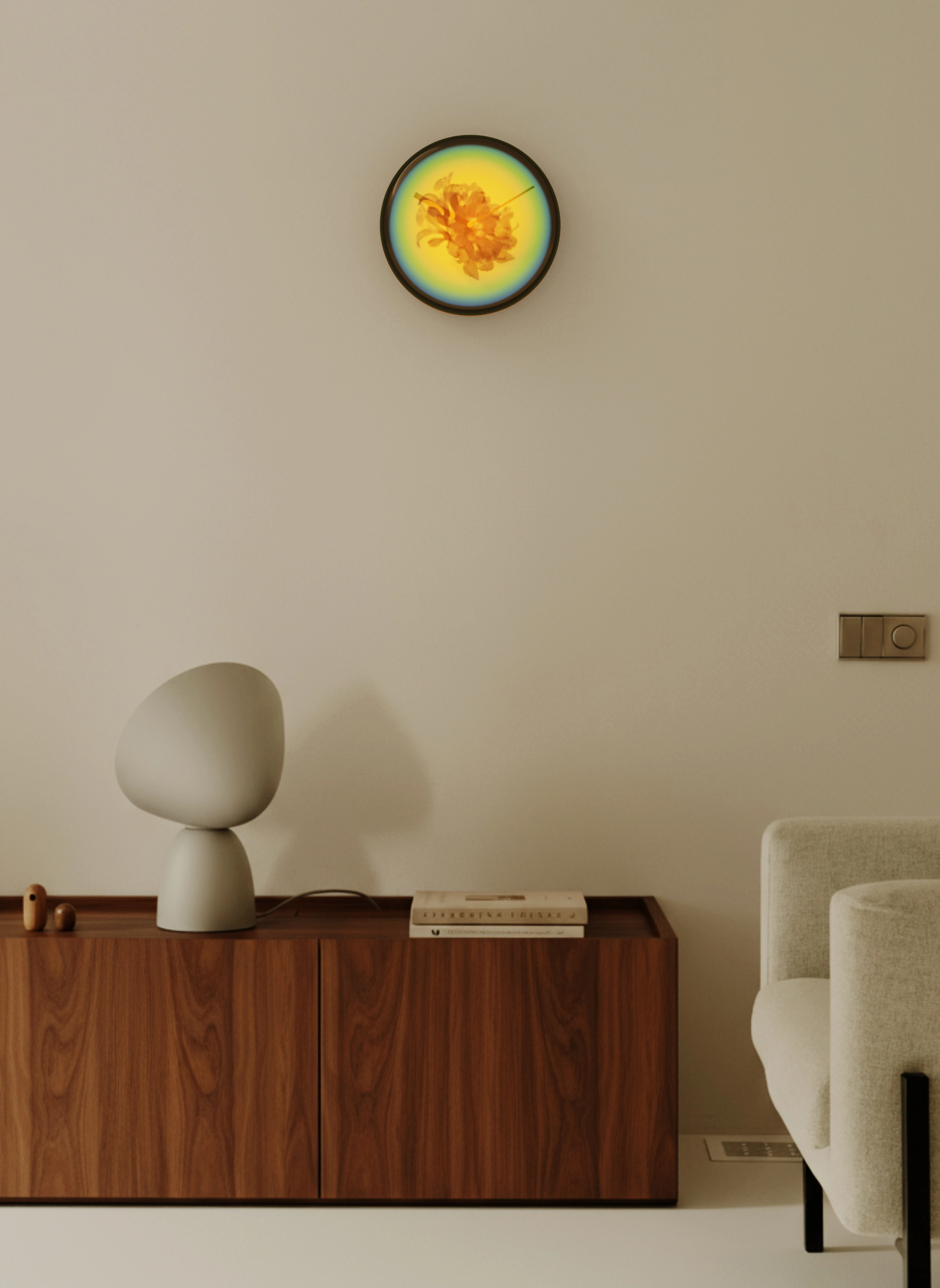 Minimalist interior with a wooden cabinet holding a modern gray lamp and two stacked books, a beige sofa on the right, and a round wall clock with yellow and blue gradient and flower design.