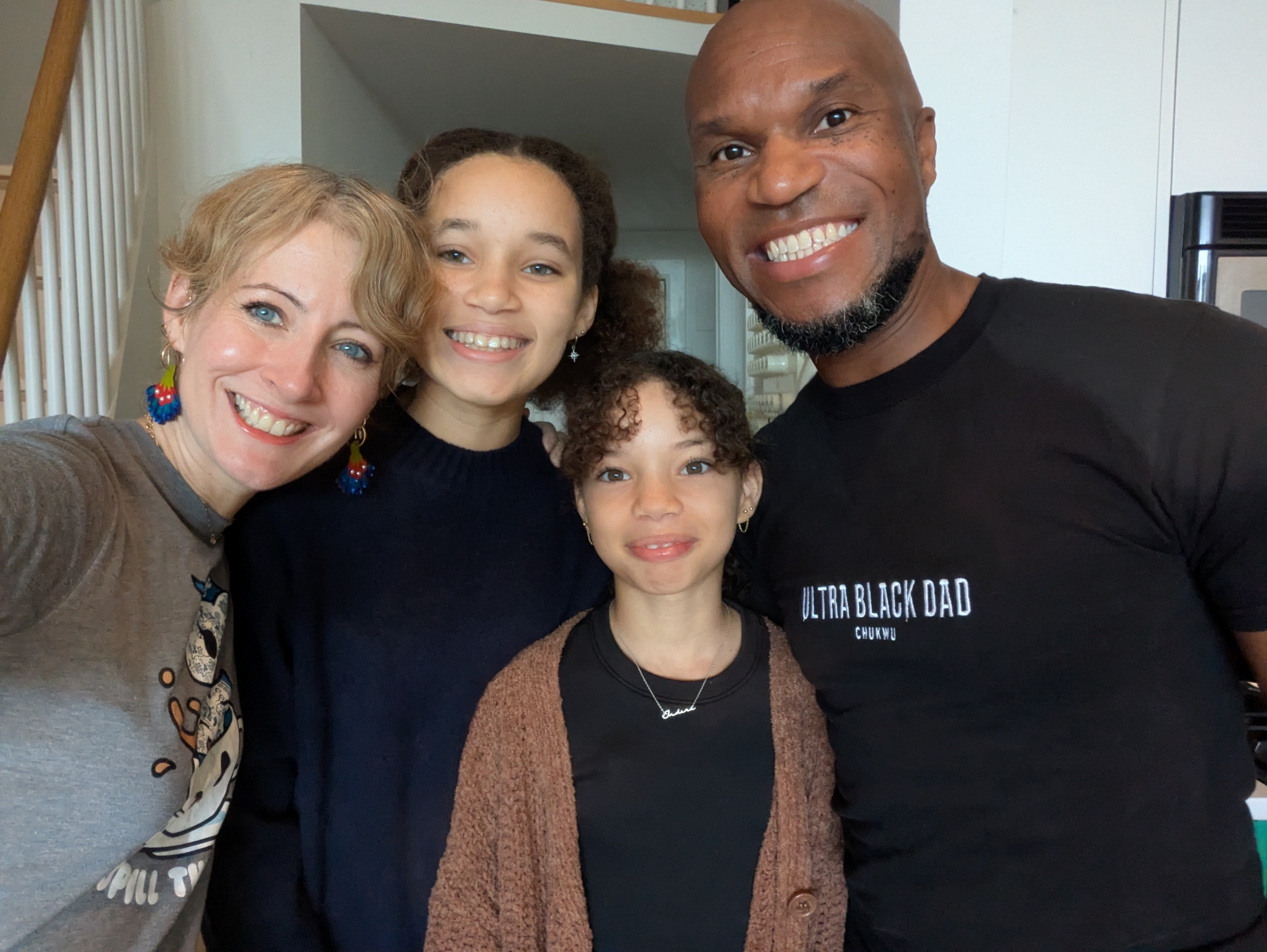 Four people engaged in conversation indoors, one man wearing a sweatshirt that says 'READ BOOKS DRINK COFFEE FIGHT EVIL.'
